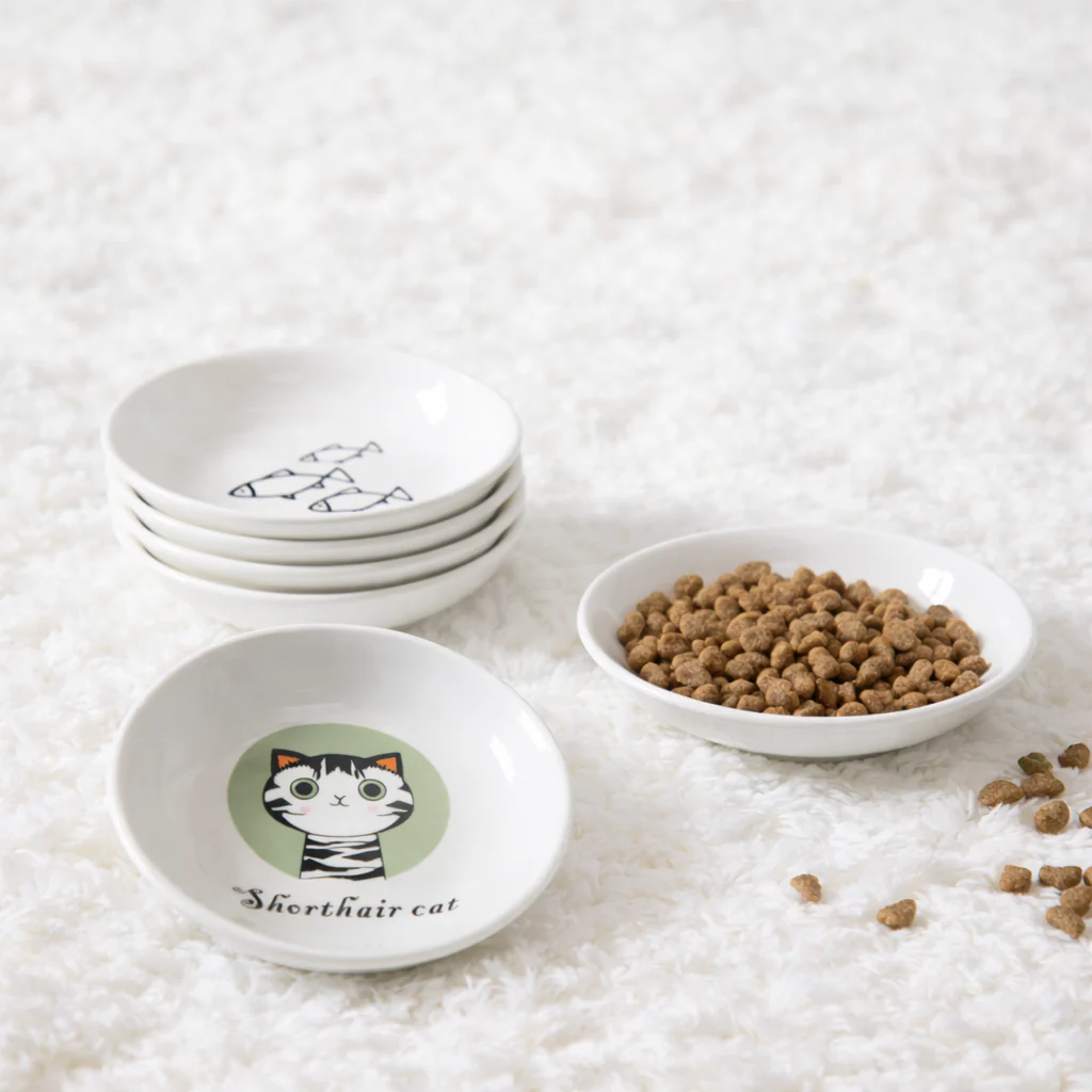 Set of white bowls with cat illustrations on a textured surface with cat food.